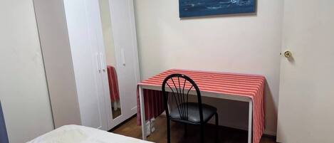 A bedroom with a bed, a desk with a chair, a wardrobe, and a painting on the wall.