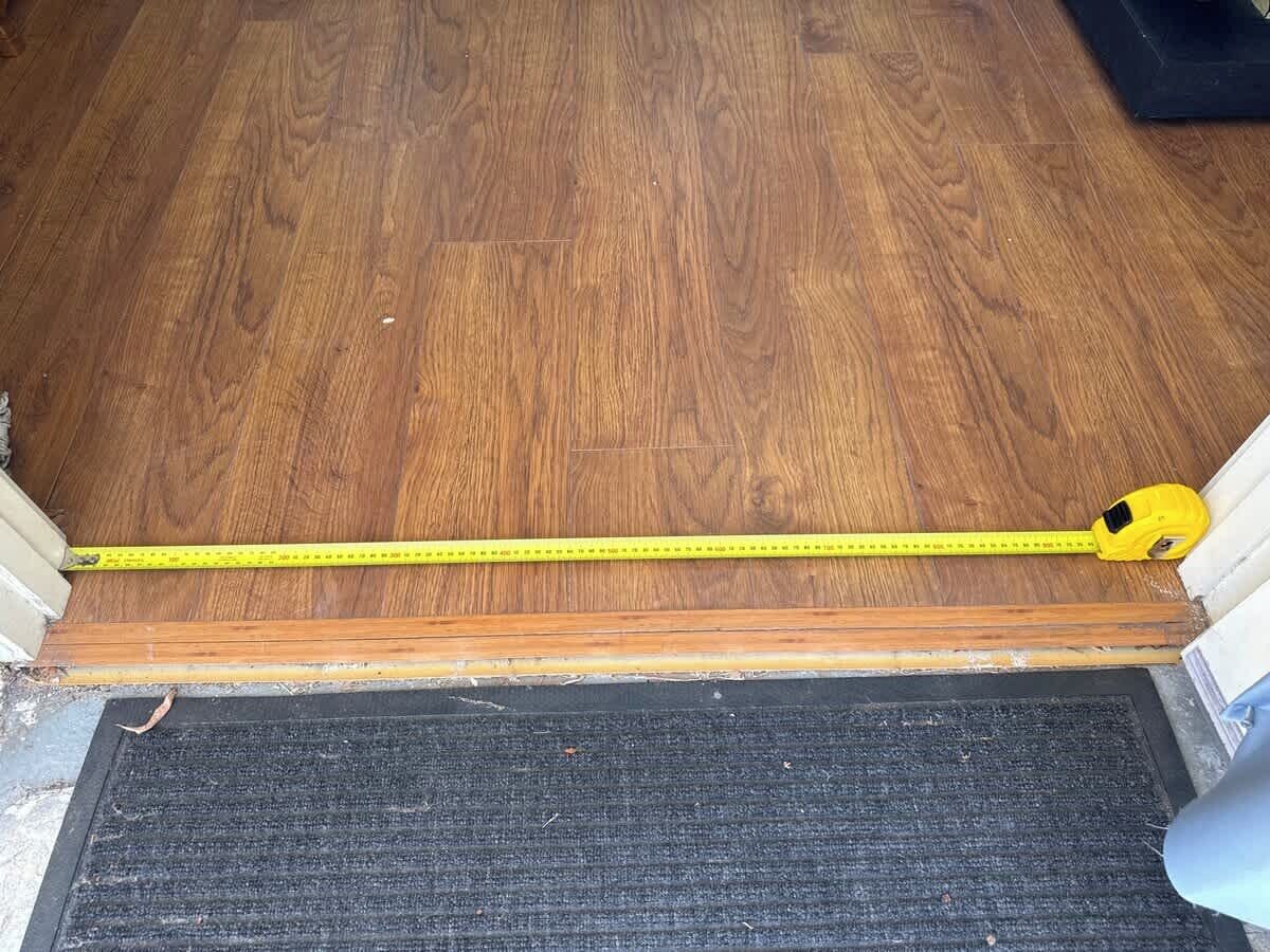 A wooden floor with a yellow measuring tape across it.