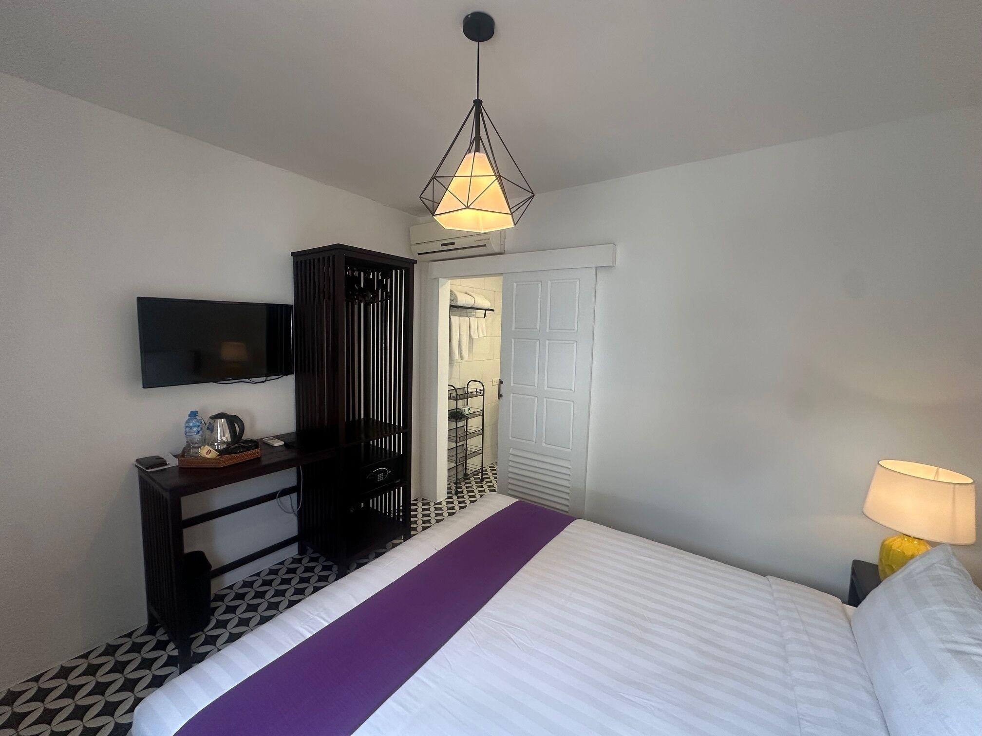 Ein Hotelzimmer mit Bett, Fernseher, Kleiderschrank, Schreibtisch mit Lampe und einer Badezimmertür.