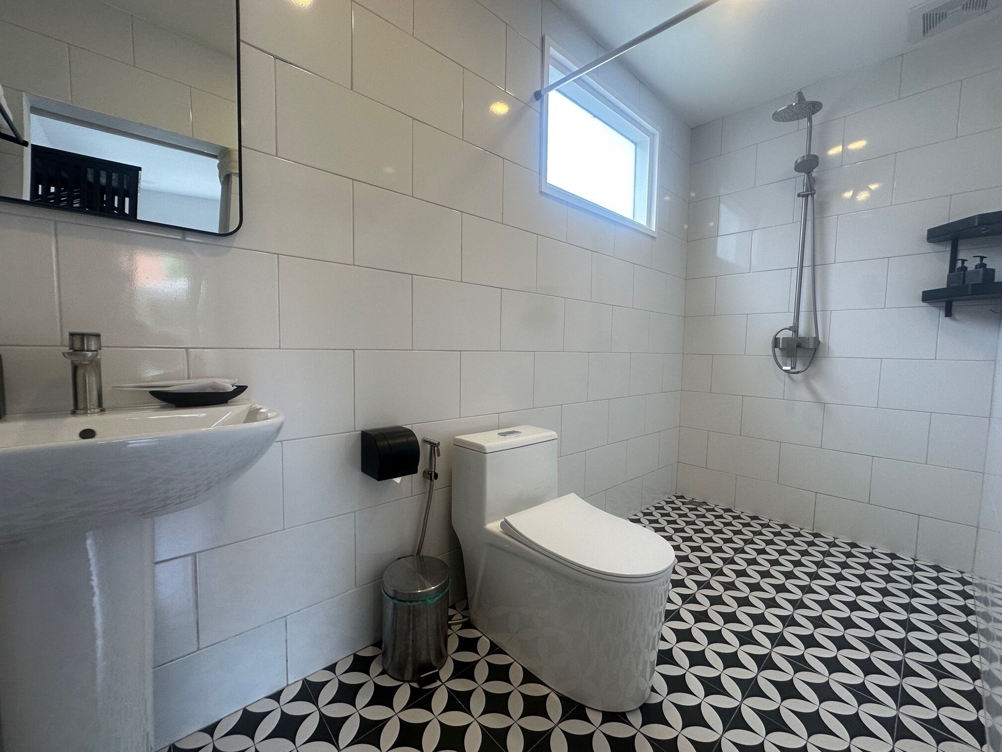 A bathroom with a white sink, toilet, and shower. The floor has a black and white geometric pattern.