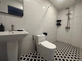 A modern bathroom with a white sink, toilet, and shower. The floor has a black and white geometric tile pattern.