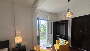 Een kamer met een bed, een lamp, twee gele stoelen, een zwarte boekenkast en een deur die leidt naar een balkon.