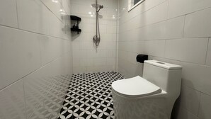 Een badkamer met witte tegels, een zwart-wit vloertegelpatroon, een toilet en een douche met een handdouche.