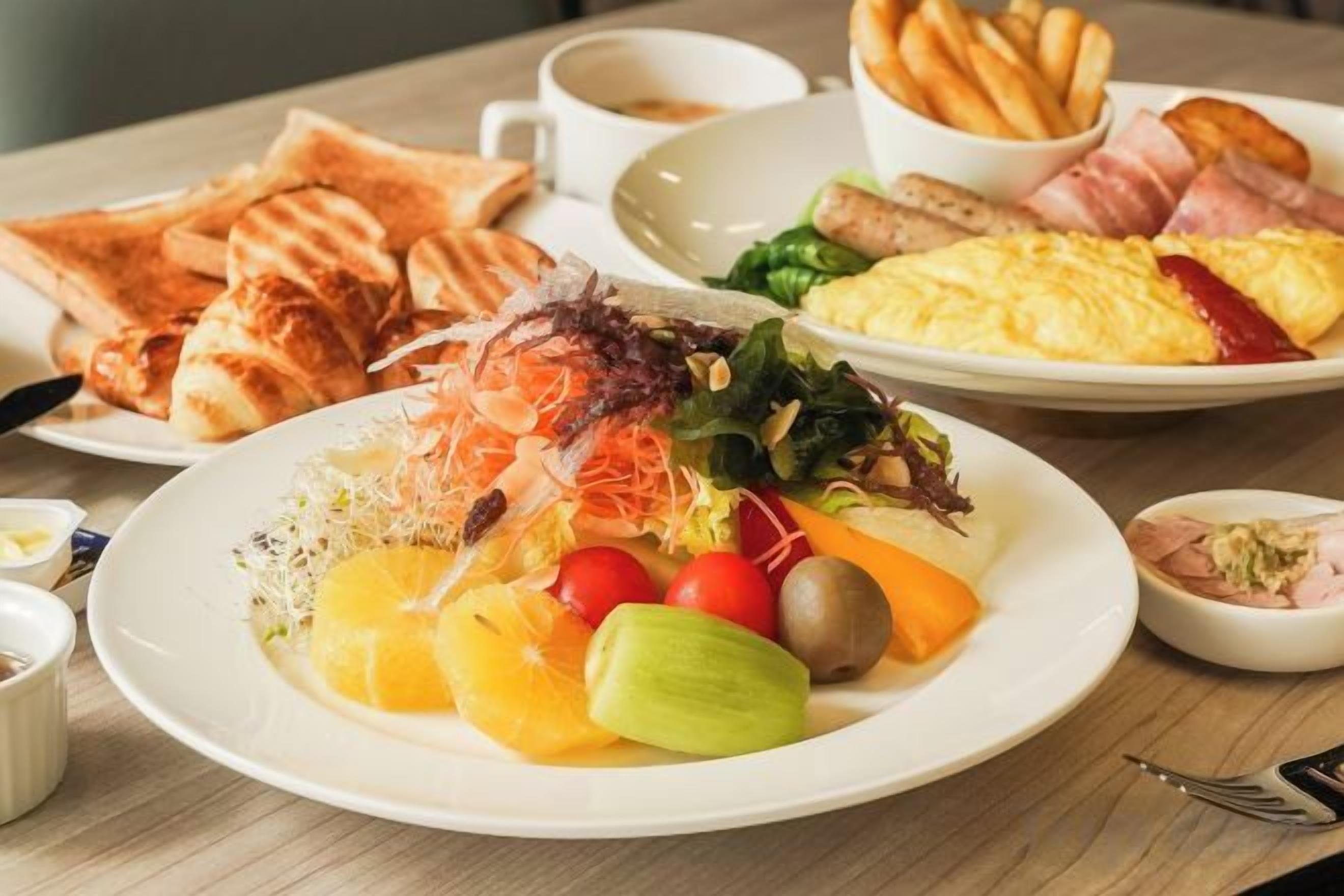 A breakfast setting with toast, eggs, ham, and a variety of fruits and vegetables on a table.