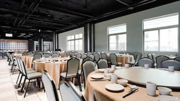 Un salón de conferencias con varias mesas y sillas, ventanas amplias y un techo alto.