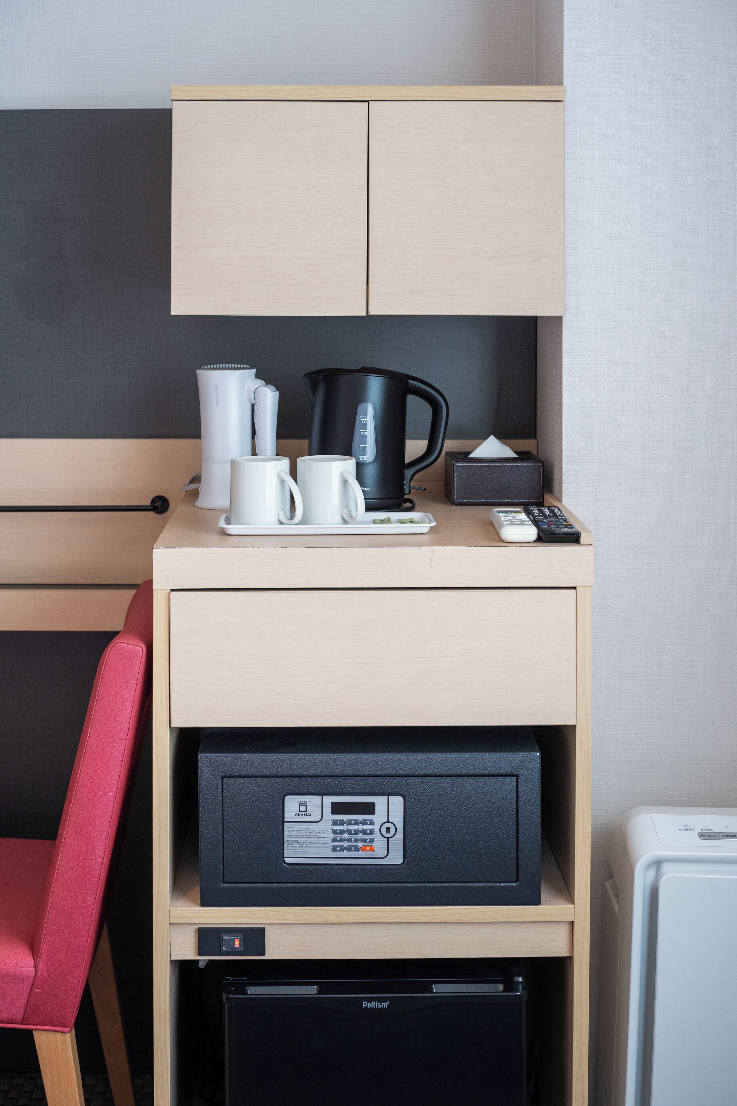 A hotel room with a kitchenette, a coffee maker, a kettle, a remote control, and a printer.