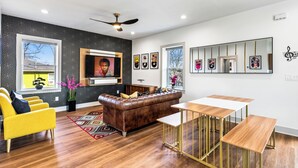 Una sala moderna con un sofá de cuero marrón, sillones amarillos, una mesa de comedor de madera y un televisor de pantalla plana grande montado en la pared.