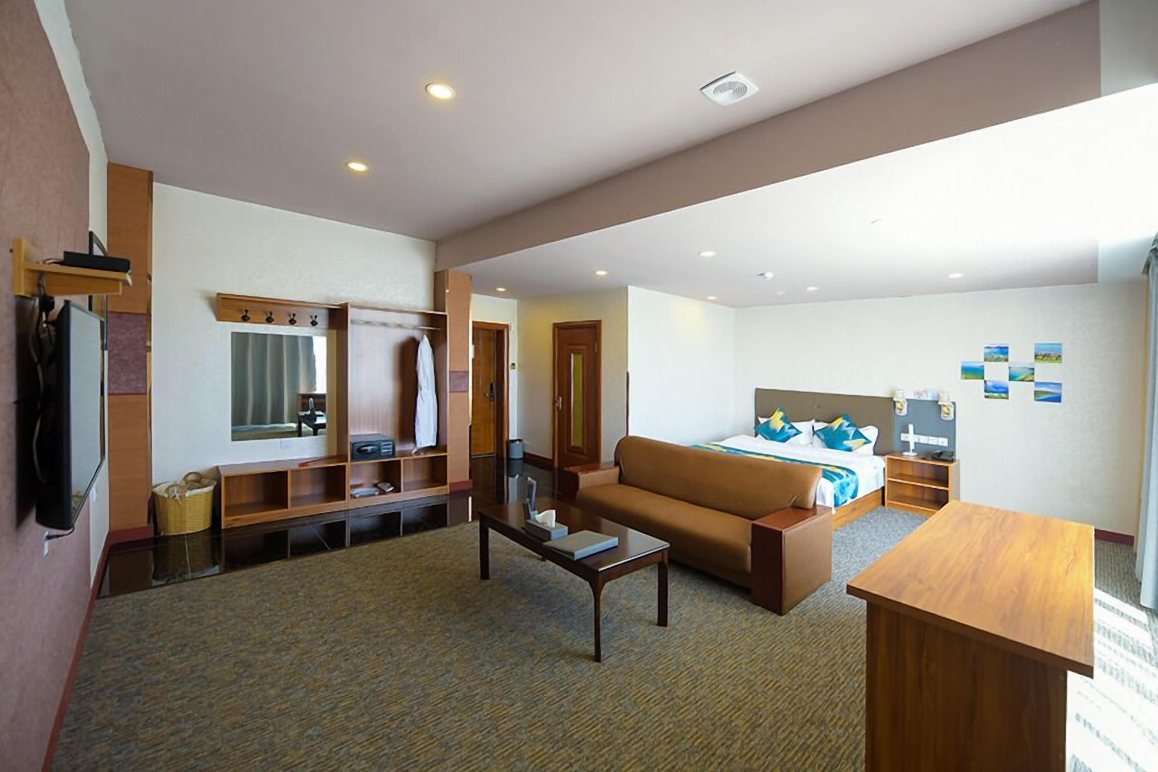 A hotel room with a living area, a bed, a TV, a desk, and a bathroom.