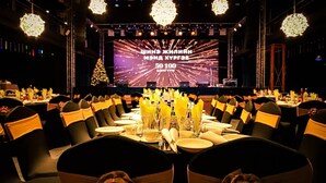 Un comedor formal con mesas redondas, sillas negras con fajos amarillos y una pantalla grande que muestra texto en escritura cirílica.