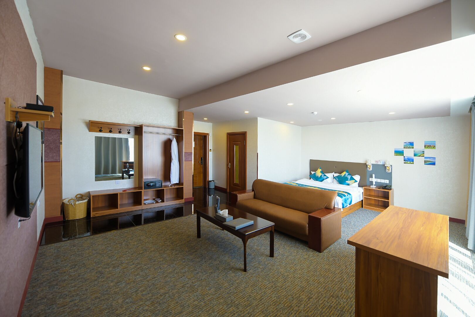 Habitación de hotel con sofá, una mesita, cama con colcha azul y blanca, escritorio de madera, televisor, armario y espejo.