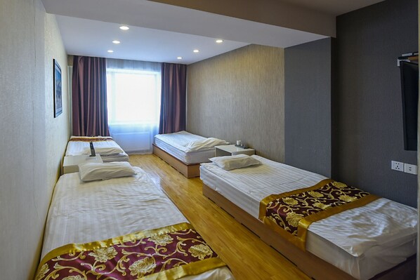 A hotel room with four single beds, a large window with curtains, and a flat-screen TV mounted on the wall. - V Hotel & Event Hall (Moron)