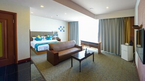 Una habitación de hotel con cama, sofá marrón, mesa de centro, escritorio y televisor.