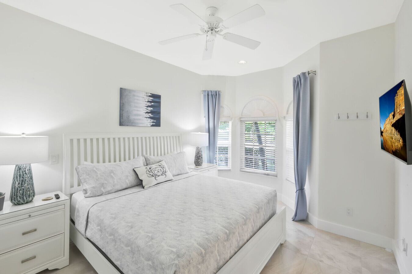 A bedroom with a bed, nightstands, a ceiling fan, a window with curtains, and wall art.
