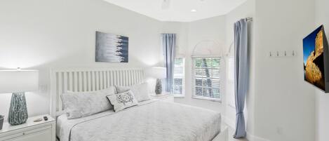 A bedroom with a bed, nightstands, a ceiling fan, a window with curtains, and wall art.