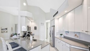 A modern kitchen with white cabinetry, a stainless steel refrigerator, and a built-in island with a sink. - Villa Blu- SW Cape Coral- Sleeps 10- Gulf Access Heated Pool Home (Cape Coral)