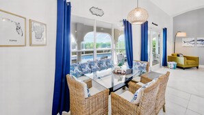 A modern dining area with a glass table, wicker chairs, and blue curtains. - Villa Blu- SW Cape Coral- Sleeps 10- Gulf Access Heated Pool Home (Cape Coral)