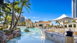 Ein Poolbereich eines Resorts mit Palmen, Liegestühlen und wolkenlosem, blauem Himmel.