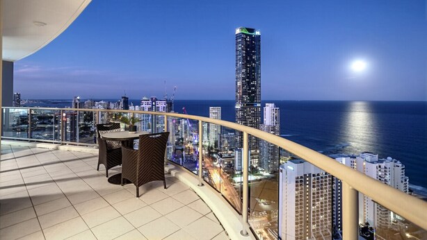 Ein Balkon mit Blick auf eine Stadtlandschaft und das Meer bei Einbruch der Dämmerung.
