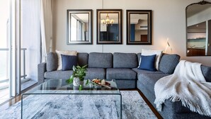 Ein modernes Wohnzimmer mit einem grauen Ecksofa, einem Glastisch mit Pflanze und drei gerahmten Spiegeln an der Wand.