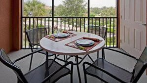 A round table with four chairs on a balcony, overlooking a scenic view of trees and a distant landscape.