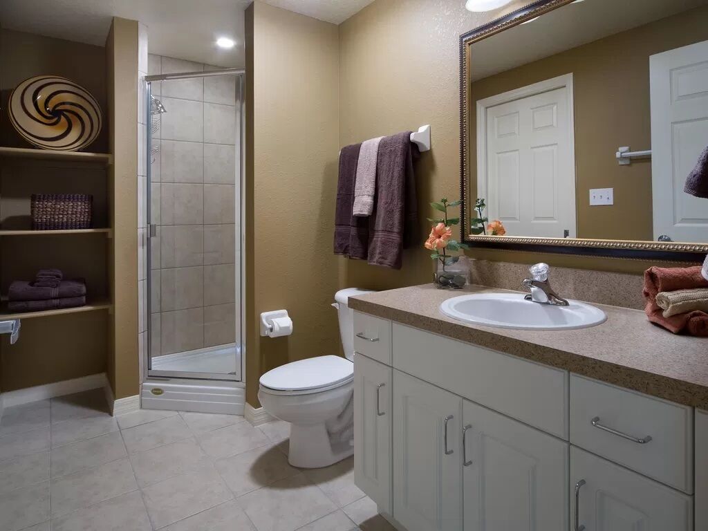 A bathroom with a shower, toilet, sink, and a large mirror.