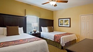 A hotel room with two beds, a desk, a ceiling fan, a framed picture on the wall, and a door.
