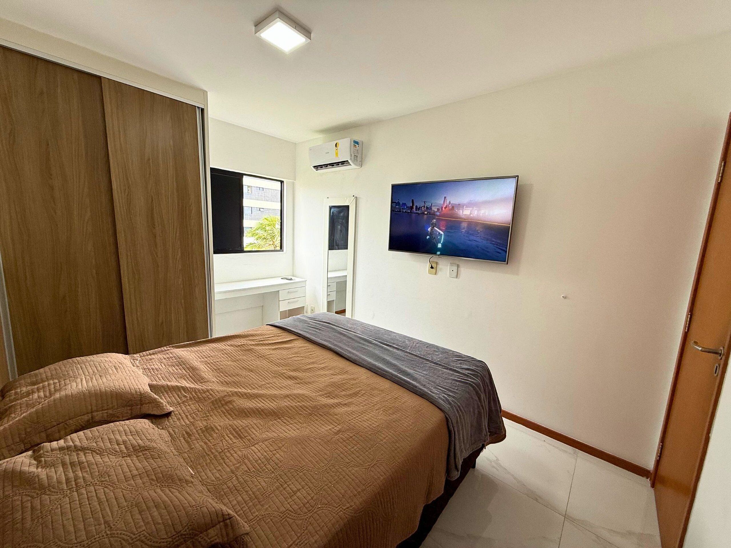 Un dormitorio con cama, televisión montada en la pared, armario y ventana.