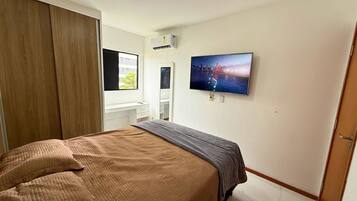 Un dormitorio con cama, televisión montada en la pared, armario y ventana.