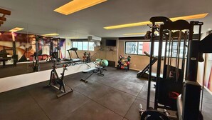 Et fitnessrum med forskellig træningsudstyr, et stort spejl og et vindue med udsigt ud.