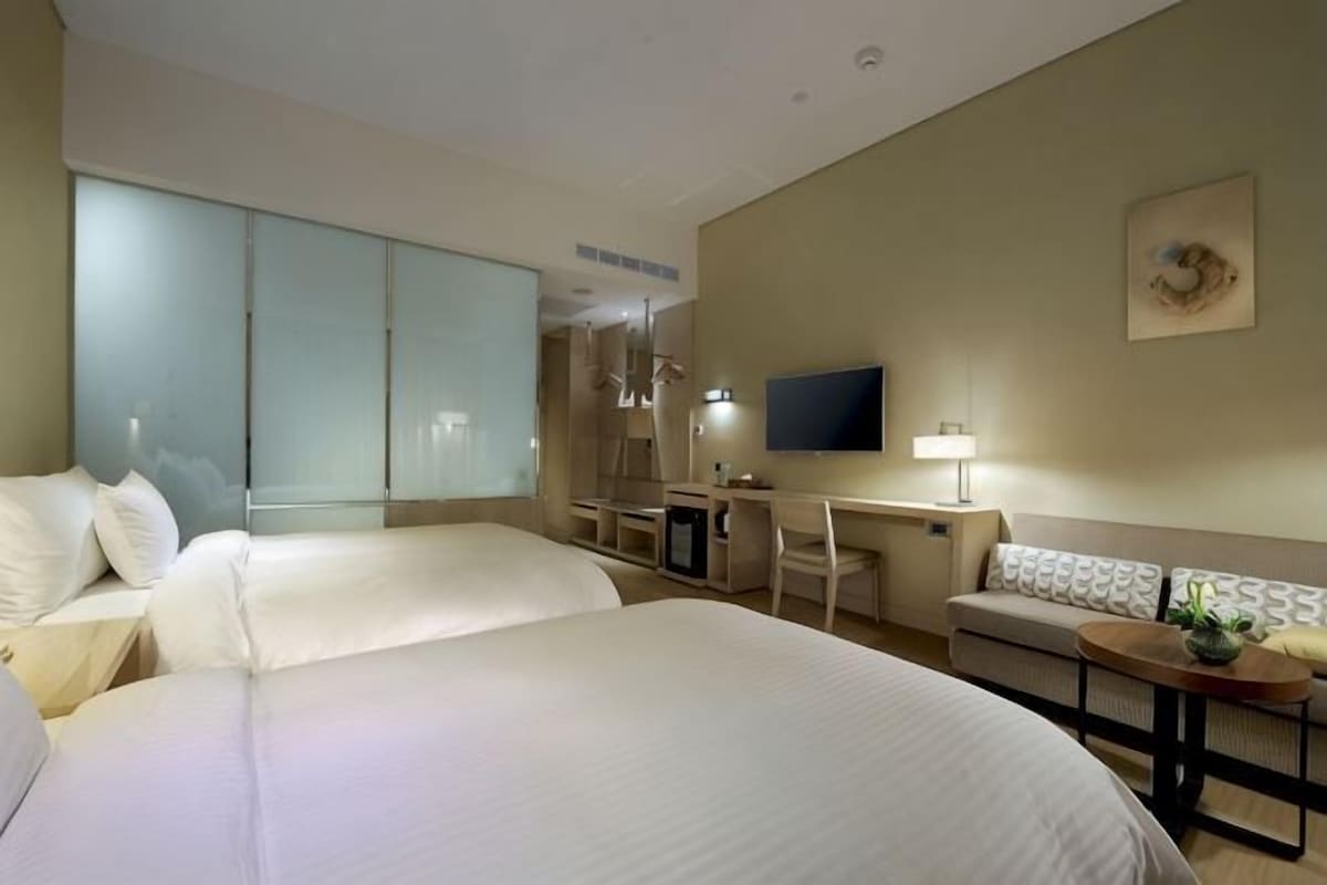 A hotel room with two beds, a desk, a TV, and a sofa.