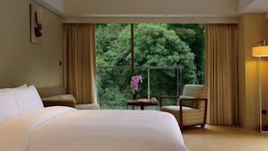 A hotel room with a large bed, a chair, a small table, and a view of trees through a window. - Century Hotel (Taitung)