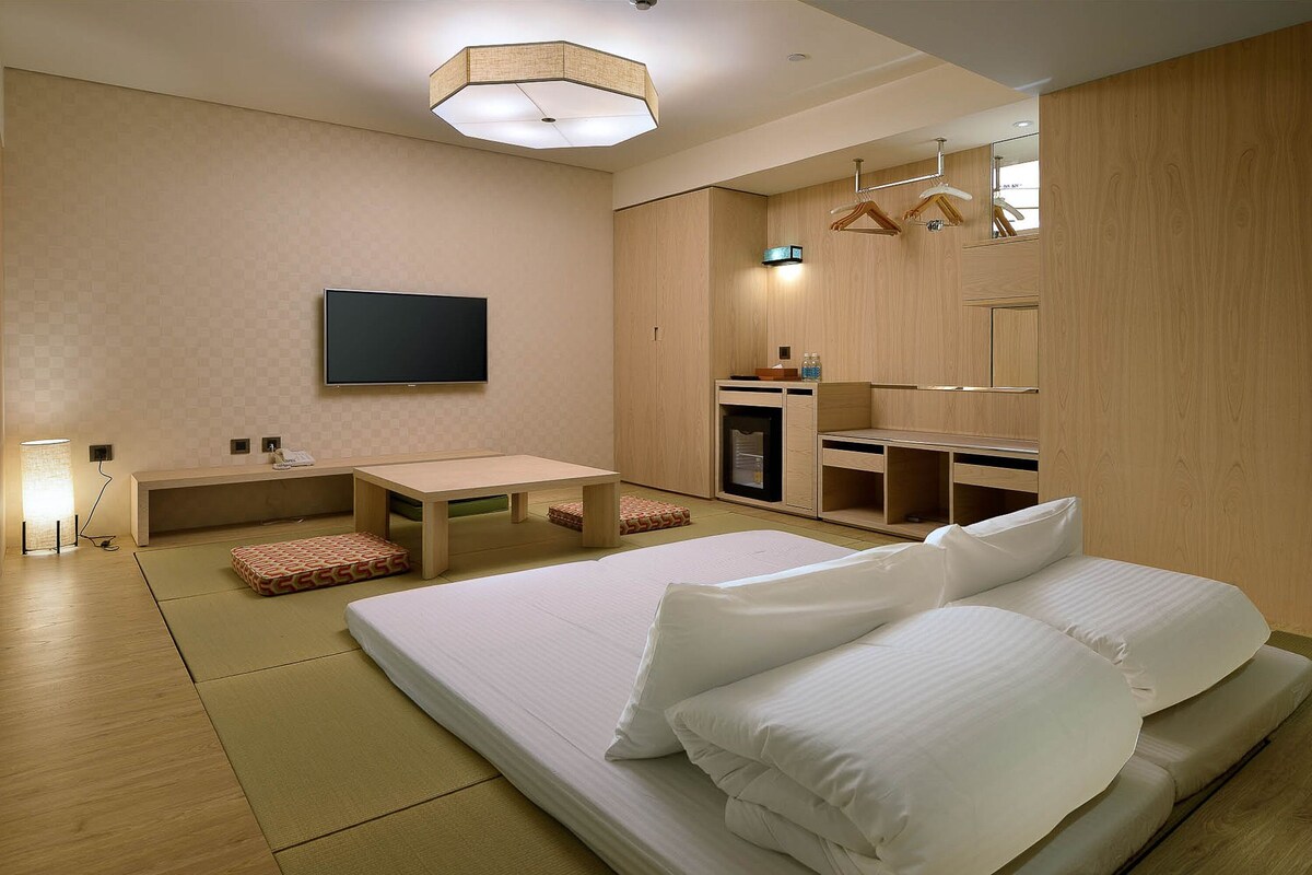 A modern hotel room with a large bed, a flat-screen TV, a desk, and a mirror.