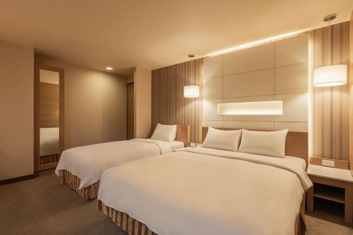 A hotel room with two beds, a wooden headboard, and bedside lamps.