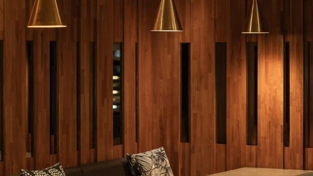 Una habitación con paneles de madera, un sofá con cojines estampados y tres lámparas colgantes.