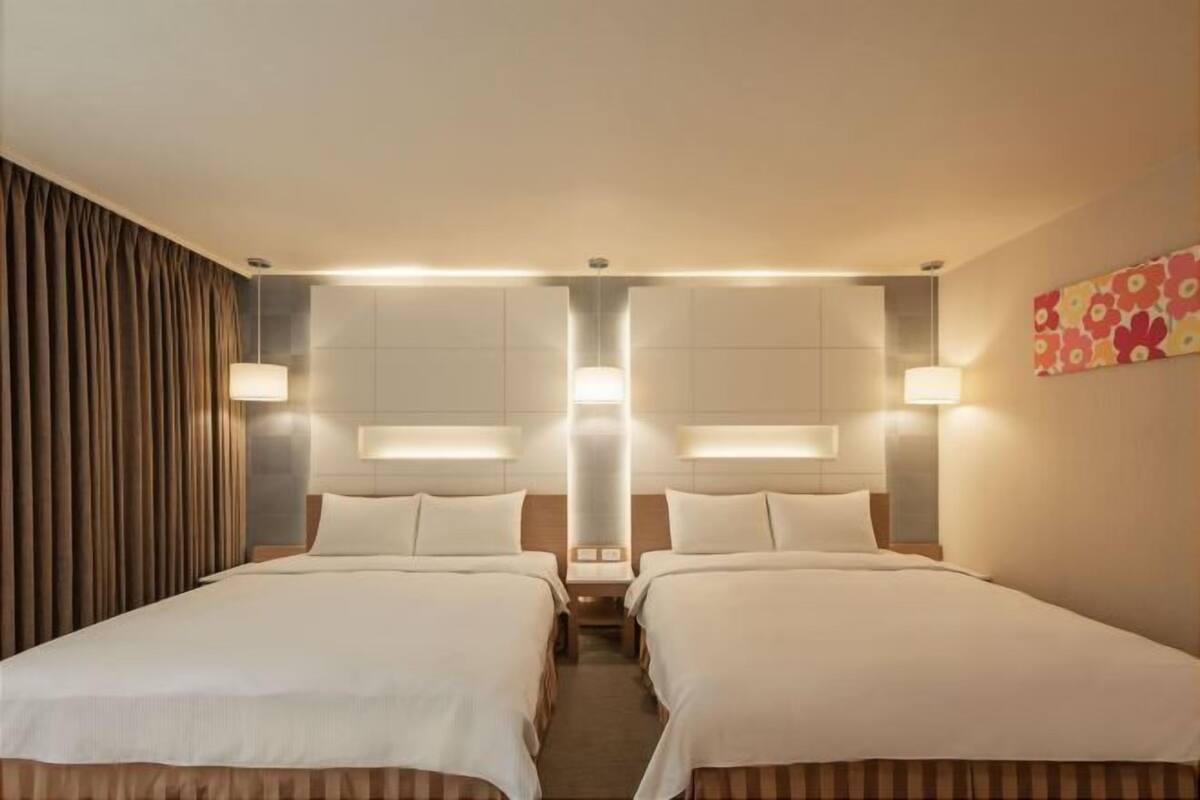 A hotel room with two beds, a large window, and a wall-mounted light fixture.