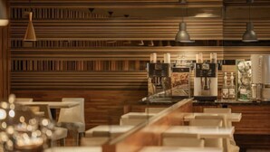 Un interior de restaurante moderno con pared de paneles de madera, iluminación colgante y una zona de bar con máquinas de café.