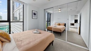 A modern hotel room with a large bed, a ceiling fan, and a view of the city through large windows. - 1Bed + Car Park Valley Spot (Brisbane)