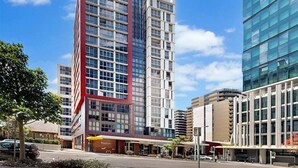 A modern hotel with a prominent red and white facade, large windows, and a visible entrance with a yellow awning. - 1Bed + Car Park Valley Spot (Brisbane)