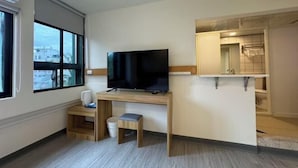 A modern hotel room with a flat-screen TV on a wooden desk, a small stool, a window with a view, and a built-in shower area. - Bantshiann Hualie Hotel (Hualien)