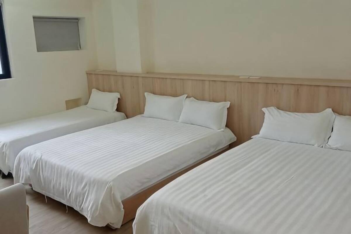 Drei Einzelbetten mit Holz Kopfteilen in einem Zimmer mit heller Wand und kleinem Fenster.