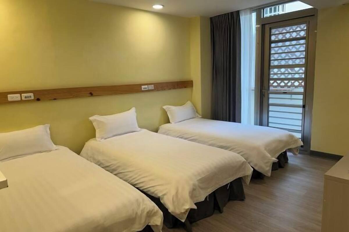 Ein Hotelzimmer mit zwei Betten, einem Holz-Kopfteil, einem Fenster mit Jalousien und einem hellen Boden.