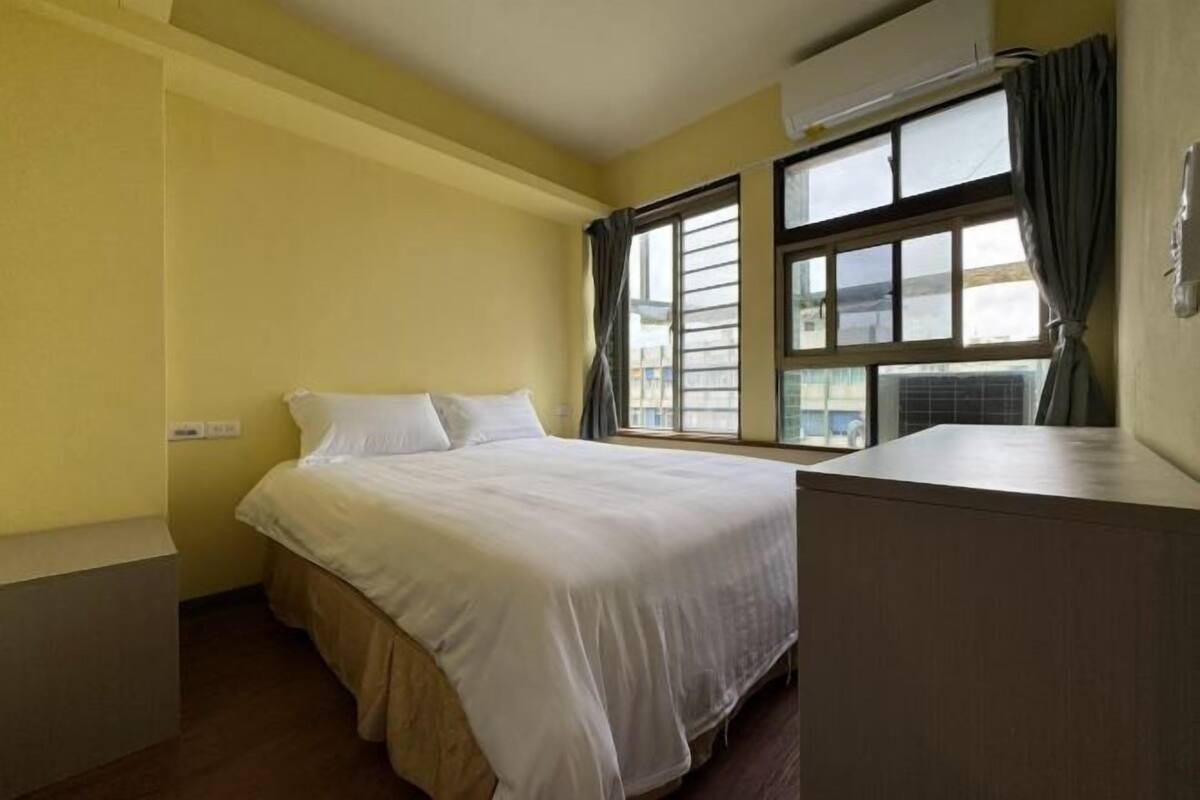 Ein Einzelbett in einem Zimmer mit gelben Wänden, einem fenster mit Vorhängen und einer Klimaanlage.