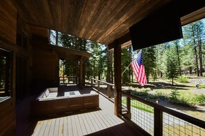 A wooden deck with a view of a forest and an American flag. - Grays Crossing Luxury Cabin w/ Spa & Putting Green (Truckee)