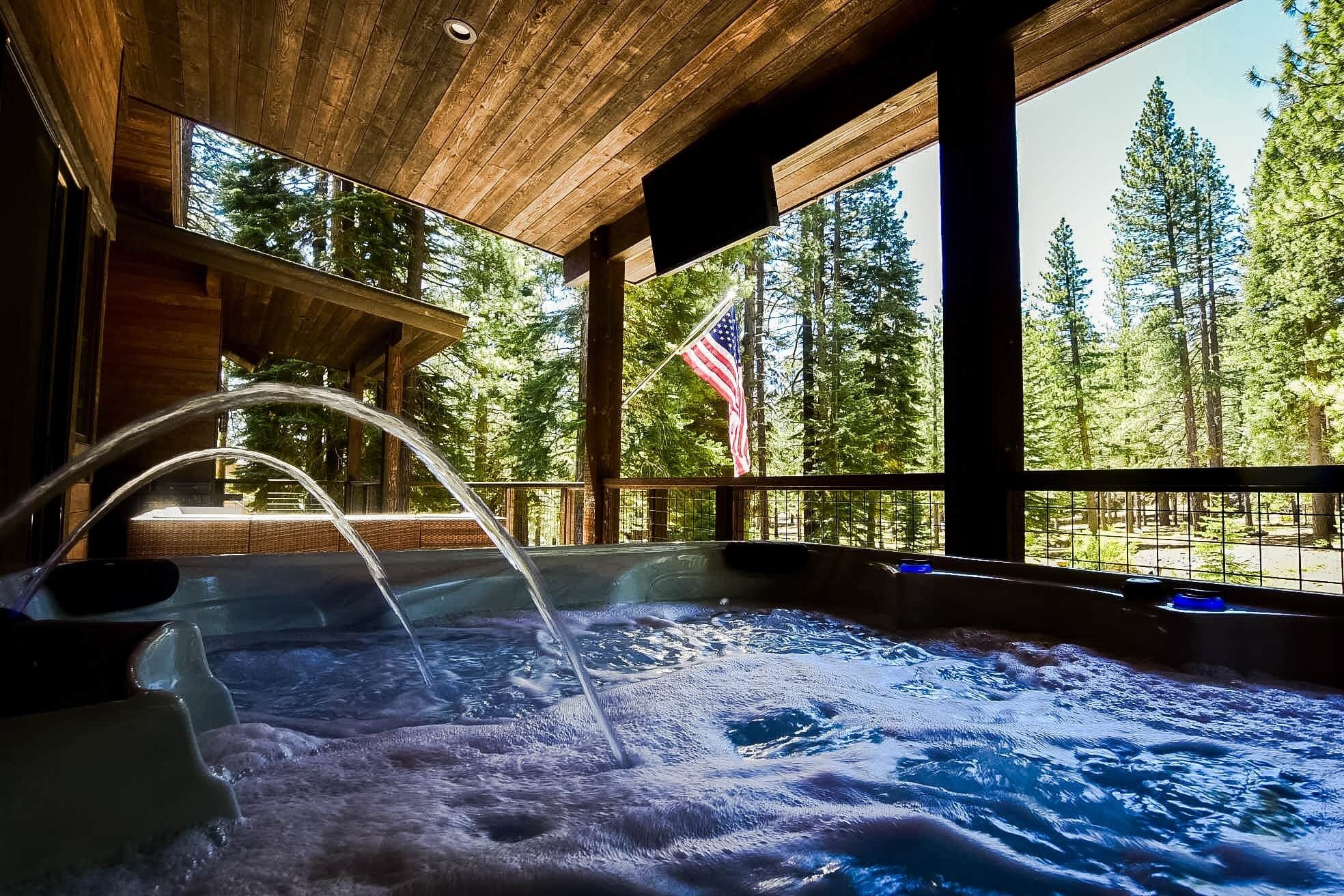 A hot tub with water jets, surrounded by wooden beams and large windows overlooking a forest.