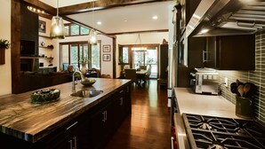A modern kitchen with a central island, stainless steel appliances, and a dining area with natural light. - Grays Crossing Luxury Cabin w/ Spa & Putting Green (Truckee)