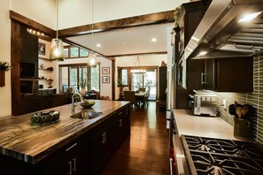 A modern kitchen with a central island, stainless steel appliances, and a dining area with natural light. - Grays Crossing Luxury Cabin w/ Spa & Putting Green (Truckee)