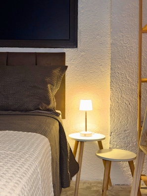 Ein ordentlich bezogenes Bett mit Kopfteil, einer Nachttischlampe und einem kleinen runden Tischchen mit Lampe.