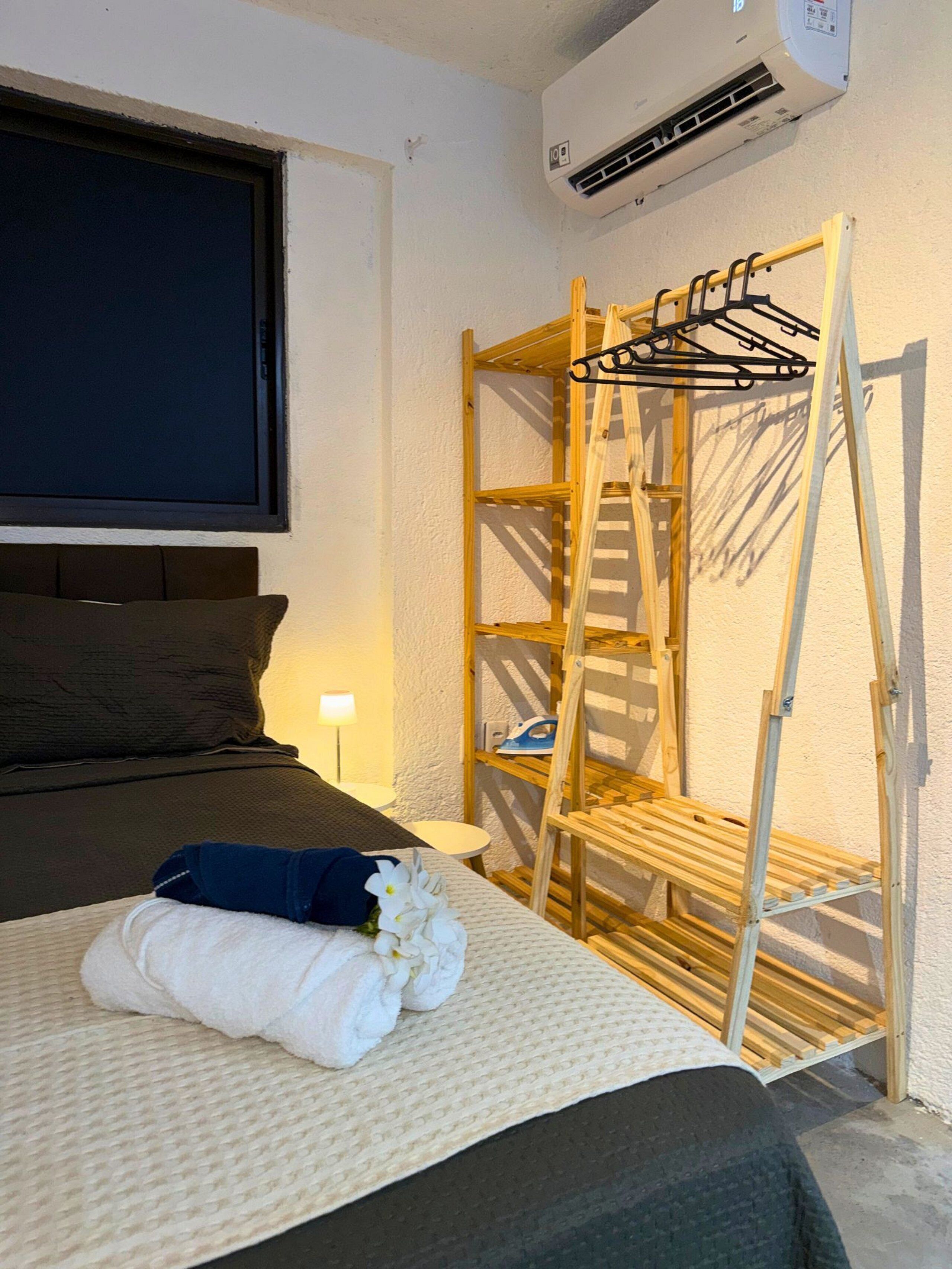 A bedroom with a bed, a wooden ladder, a wall-mounted air conditioner, and a window.