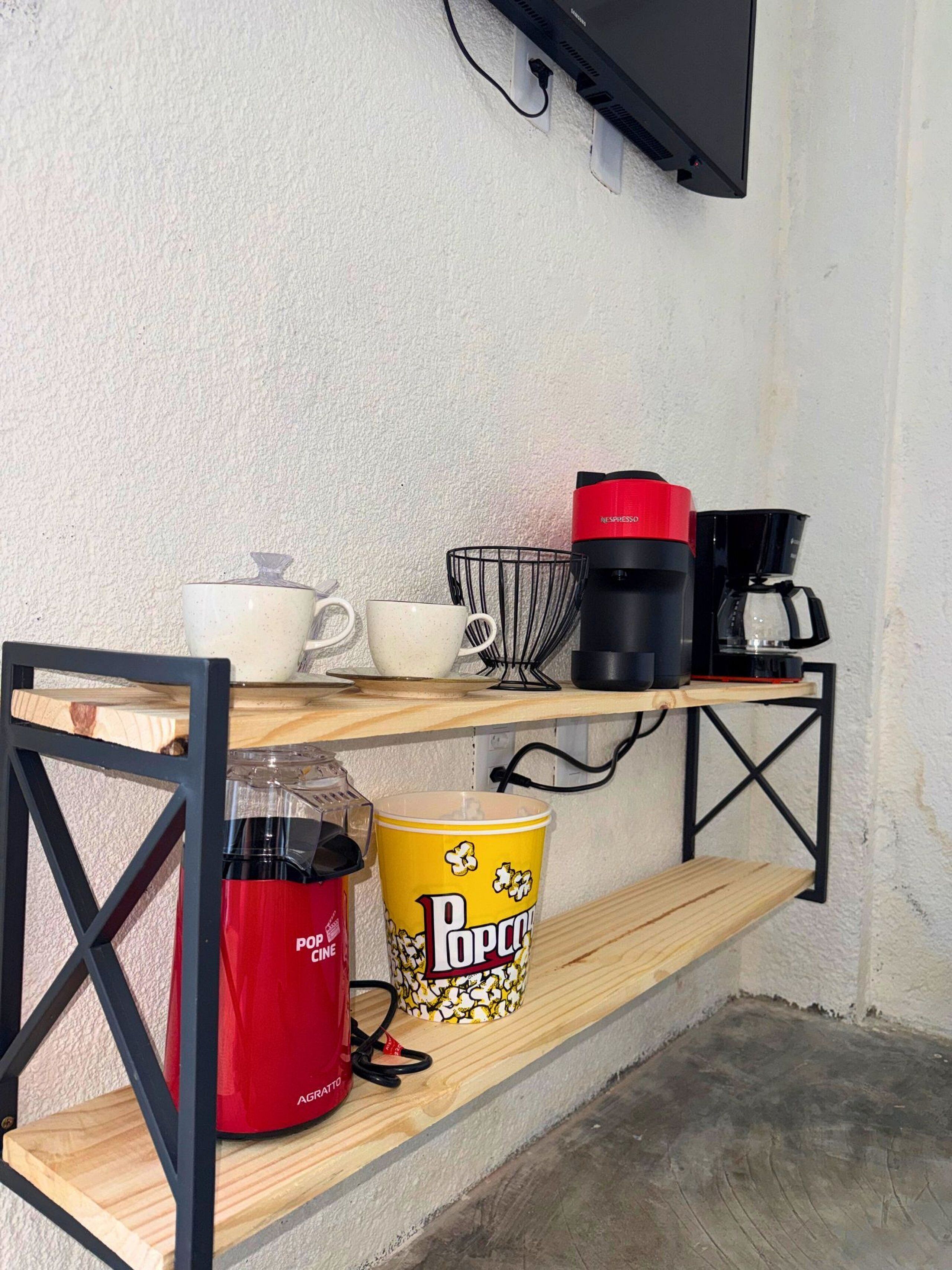 Een kitchenette met een koffiezetapparaat, een bak popcorn en een aan de muur bevestigde televisie.
