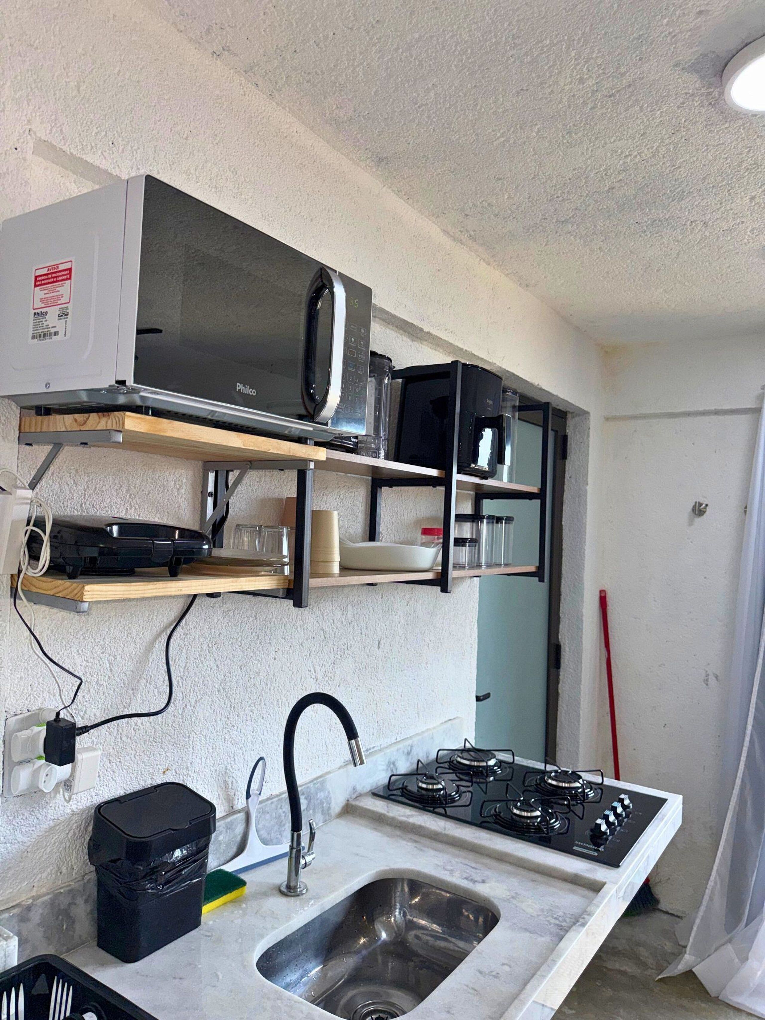 Una cucina compatta con forno a microonde integrato, piano cottura a gas e un piccolo lavandino.